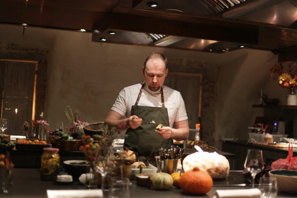 A chef at his work station in the kitchen scooping out the flesh of a fruit using a spoon.