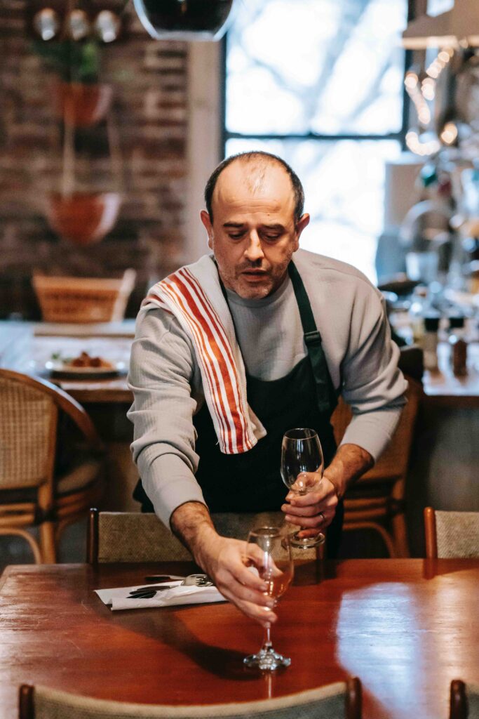 A chef laying down wine glass to create a table setting at his restaurant.