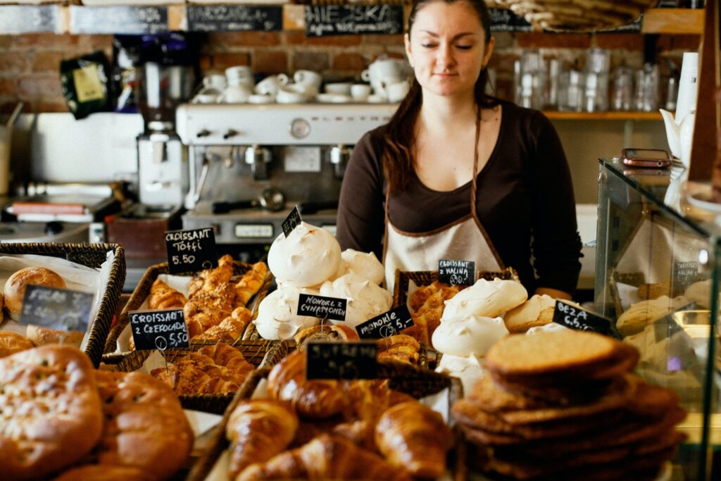 Photo of a baker standing at the counter of a café overflowing with baked goods.